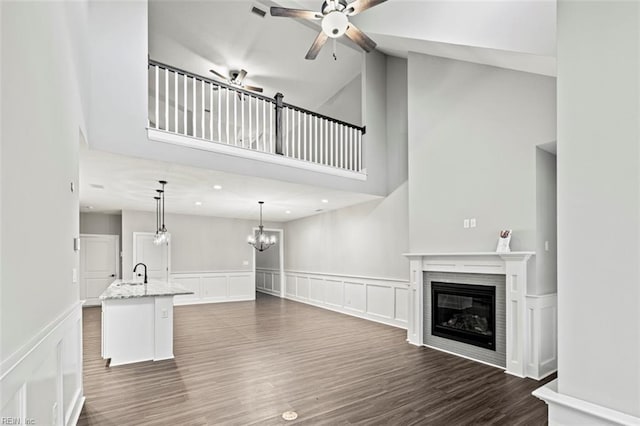 unfurnished living room featuring a glass covered fireplace, a high ceiling, a decorative wall, and ceiling fan with notable chandelier