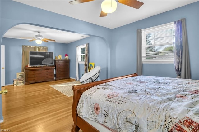 bedroom with arched walkways, a ceiling fan, and wood finished floors
