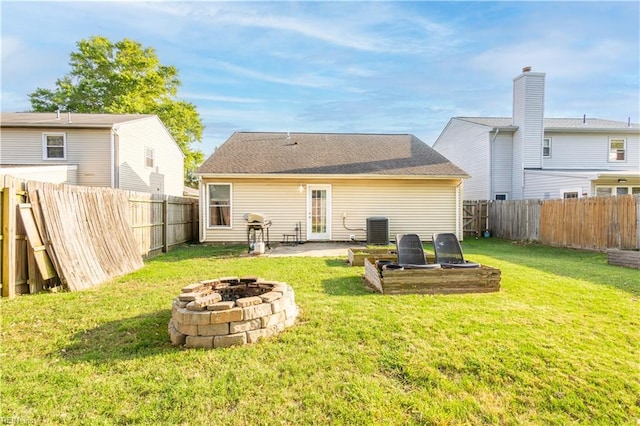 rear view of property featuring central air condition unit, a fenced backyard, a yard, and a fire pit