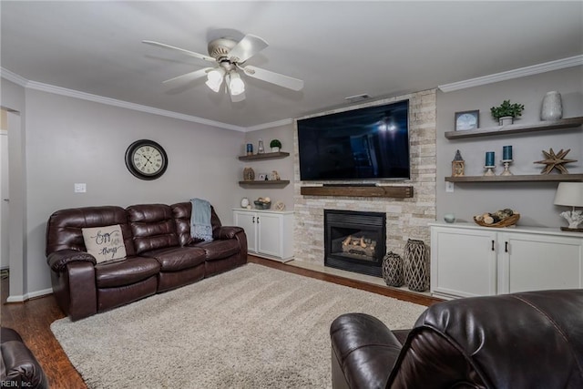 living room with crown molding, ceiling fan, a stone fireplace, baseboards, and wood finished floors