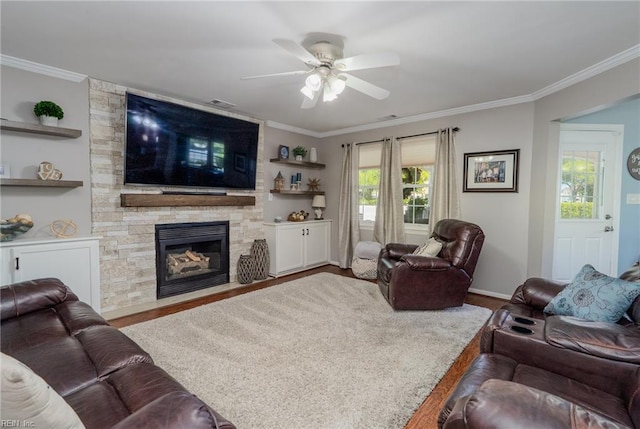 living room featuring crown molding, ceiling fan, a fireplace, baseboards, and wood finished floors