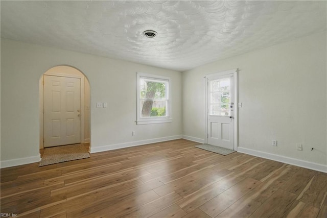 spare room with arched walkways, baseboards, and wood finished floors