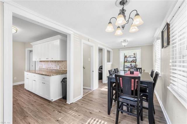 dining area with an inviting chandelier, ornamental molding, baseboards, and light wood finished floors