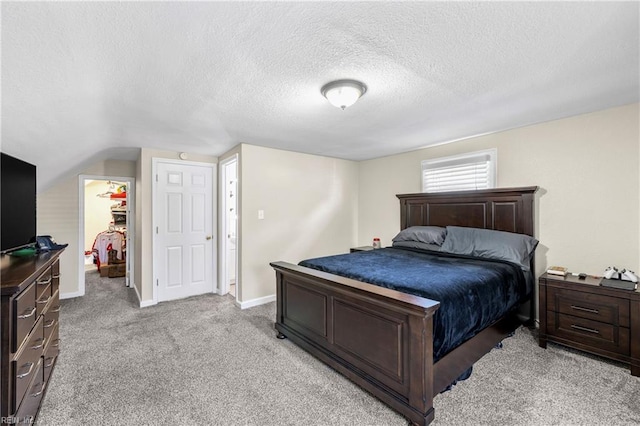 bedroom featuring light colored carpet, a textured ceiling, a walk in closet, and vaulted ceiling