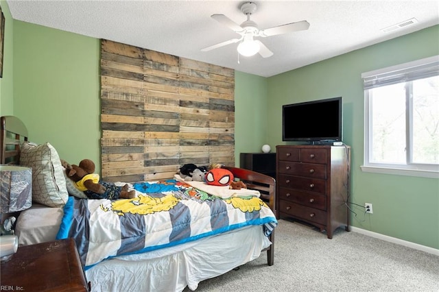 carpeted bedroom with wooden walls, ceiling fan, visible vents, and baseboards