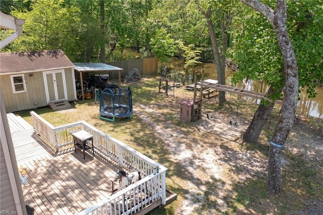 view of yard with fence, a trampoline, an outbuilding, and a deck