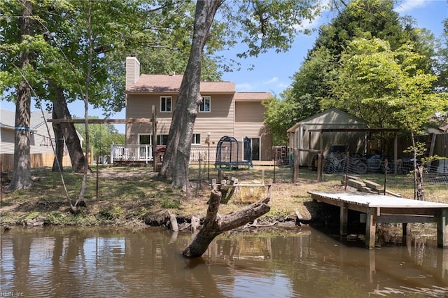 rear view of house with fence, an outbuilding, a chimney, and a deck with water view