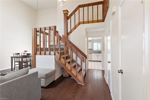 stairway featuring wood-type flooring, baseboards, and a high ceiling