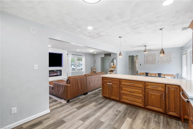 kitchen featuring light wood-style floors, open floor plan, light countertops, brown cabinets, and decorative light fixtures