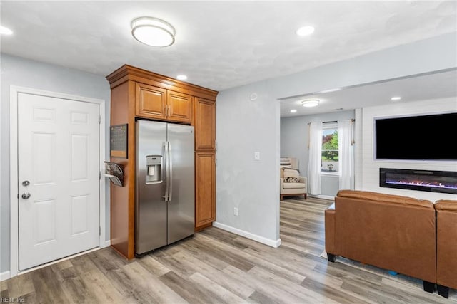 kitchen with brown cabinets, stainless steel refrigerator with ice dispenser, open floor plan, and light wood-style flooring