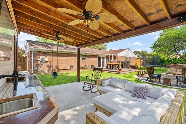 view of patio / terrace with a ceiling fan, a trampoline, an outdoor living space with a fire pit, a deck, and a sink