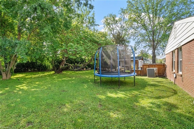 view of yard featuring fence, a trampoline, a storage shed, central air condition unit, and an outdoor structure