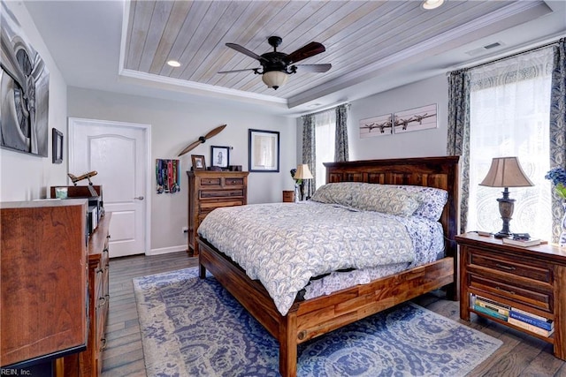 bedroom featuring crown molding, dark wood-style flooring, baseboards, ceiling fan, and a tray ceiling