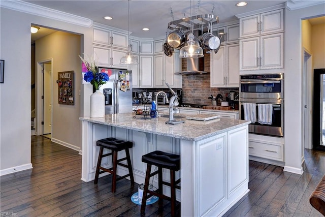 kitchen featuring dark wood finished floors, wall chimney exhaust hood, stainless steel appliances, baseboards, and tasteful backsplash