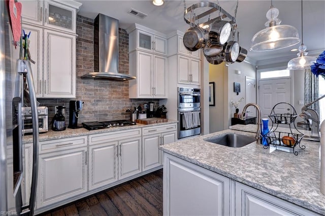kitchen with wall chimney range hood, dark wood-style flooring, visible vents, appliances with stainless steel finishes, and a sink