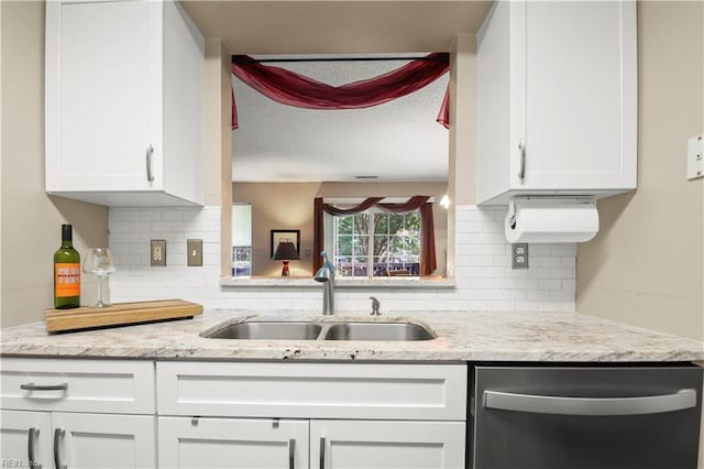 kitchen featuring stainless steel dishwasher, white cabinets, tasteful backsplash, light stone counters, and a sink