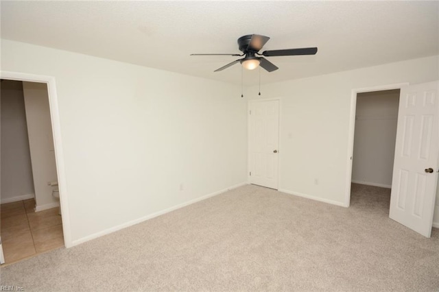 unfurnished bedroom with ceiling fan, baseboards, a closet, a spacious closet, and light carpet