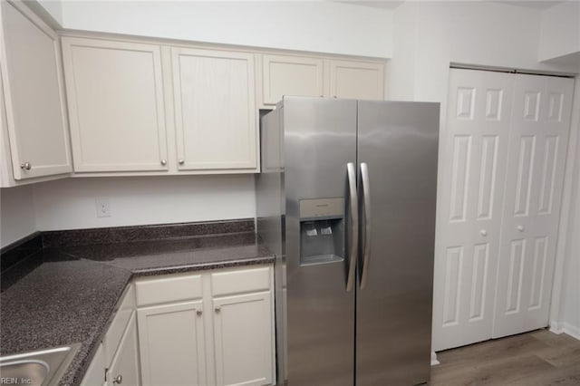 kitchen with stainless steel refrigerator with ice dispenser, a sink, dark stone counters, and wood finished floors