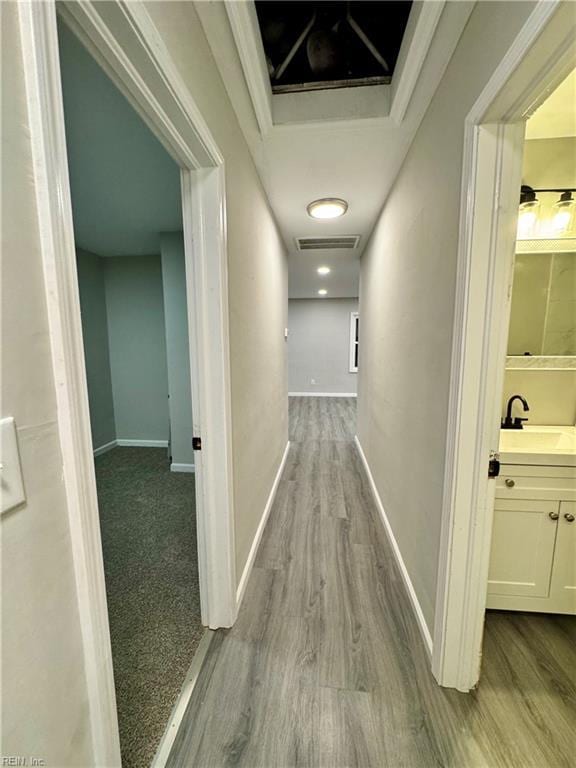 hall featuring visible vents, a sink, wood finished floors, and baseboards
