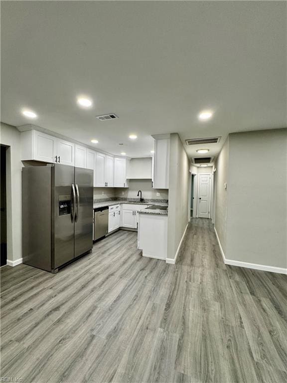 kitchen with appliances with stainless steel finishes, light wood finished floors, a sink, baseboards, and visible vents