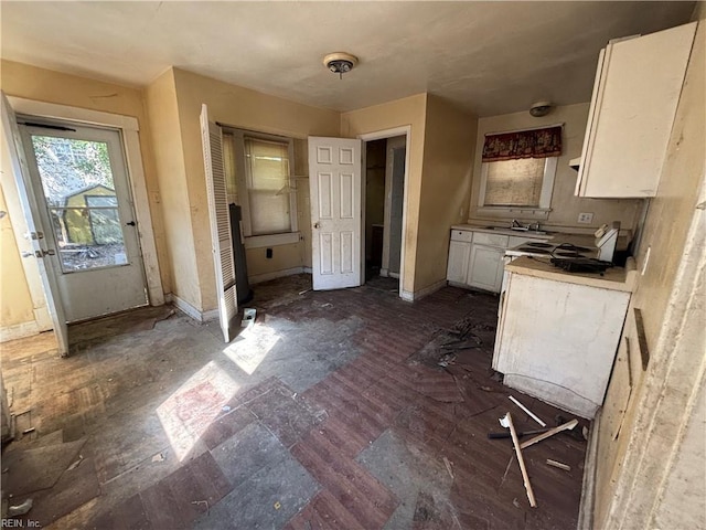 kitchen featuring baseboards, white cabinets, light countertops, and a sink