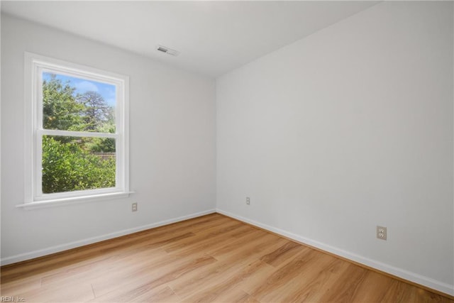 empty room featuring light wood-style floors, baseboards, plenty of natural light, and visible vents