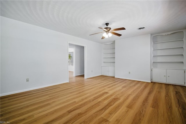 unfurnished living room featuring ceiling fan, visible vents, built in shelves, baseboards, and light wood-style floors