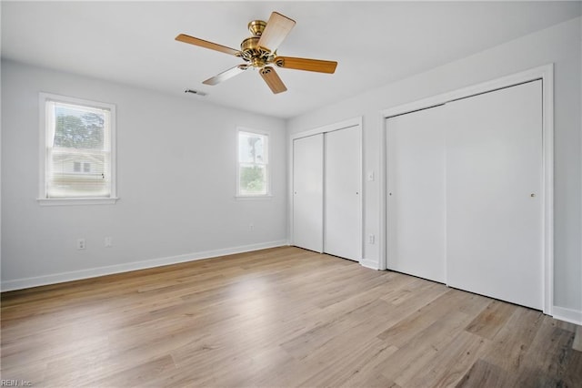 unfurnished bedroom with multiple closets, multiple windows, visible vents, and light wood-style floors