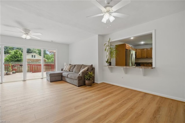 living area featuring baseboards, light wood-style flooring, and ceiling fan