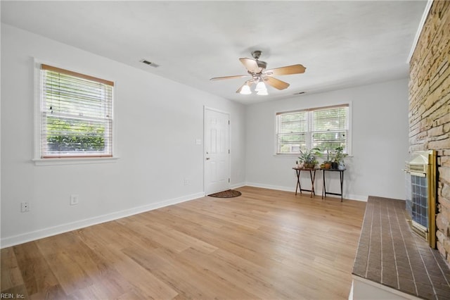 unfurnished living room with visible vents, a fireplace, baseboards, ceiling fan, and light wood-style flooring