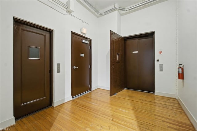 hall featuring light wood-style floors, baseboards, and elevator