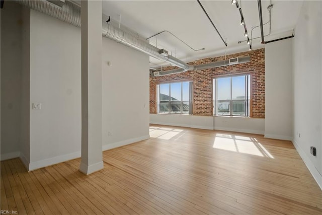 basement featuring baseboards, light wood finished floors, brick wall, and visible vents