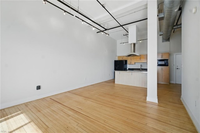 unfurnished living room with baseboards, a high ceiling, a sink, and light wood-style floors