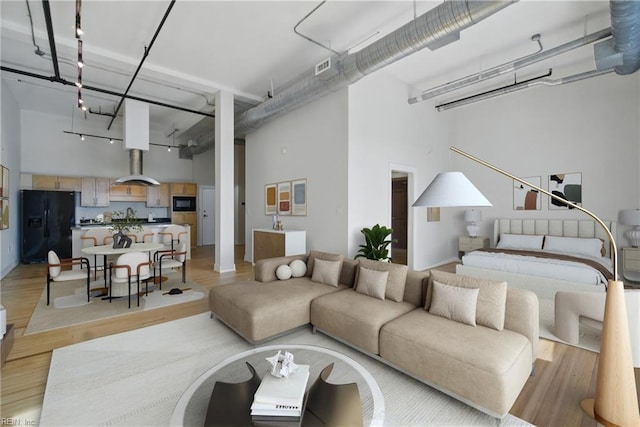 living area featuring a towering ceiling, light wood-style flooring, and visible vents