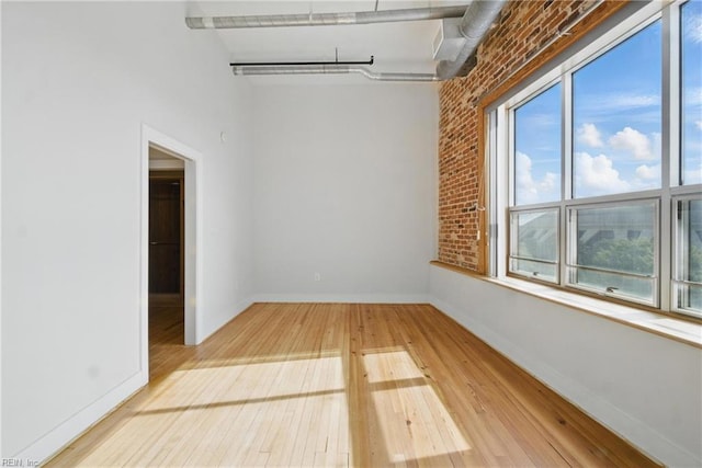 spare room featuring baseboards, hardwood / wood-style flooring, brick wall, and a towering ceiling