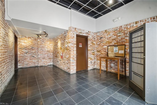 interior space featuring track lighting, a towering ceiling, tile patterned flooring, and brick wall