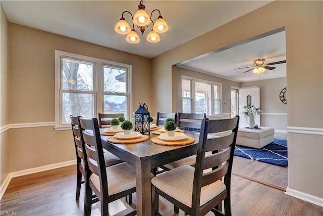 dining area with baseboards, wood finished floors, and ceiling fan with notable chandelier