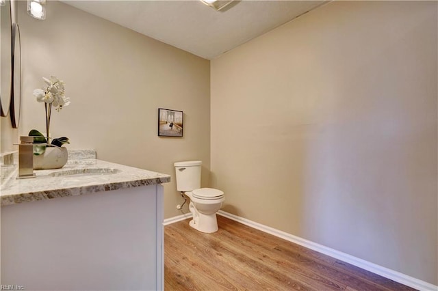 half bathroom with baseboards, wood finished floors, toilet, and vanity