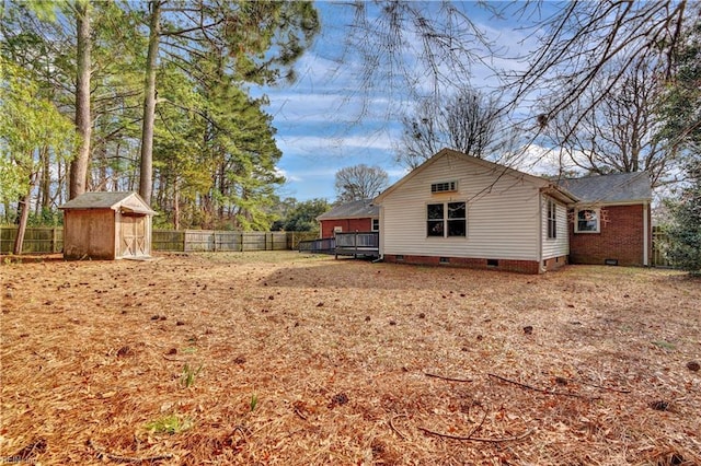 back of house with a deck, a fenced backyard, crawl space, a storage shed, and an outbuilding