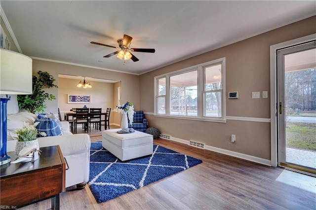 living room with ceiling fan with notable chandelier, baseboards, wood finished floors, visible vents, and ornamental molding
