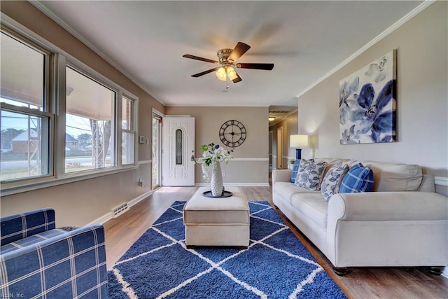 living area featuring a ceiling fan, visible vents, wood finished floors, baseboards, and ornamental molding