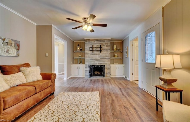 living area featuring a fireplace, built in shelves, a ceiling fan, wood finished floors, and ornamental molding