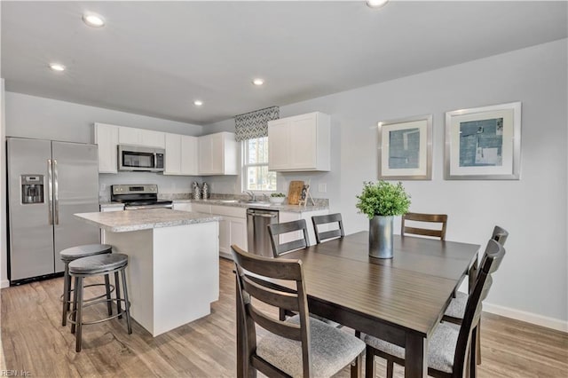 kitchen with appliances with stainless steel finishes, a center island, light countertops, a sink, and white cabinetry