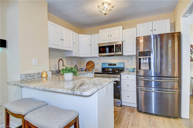 kitchen featuring white cabinets, stainless steel appliances, a peninsula, and light wood-style floors