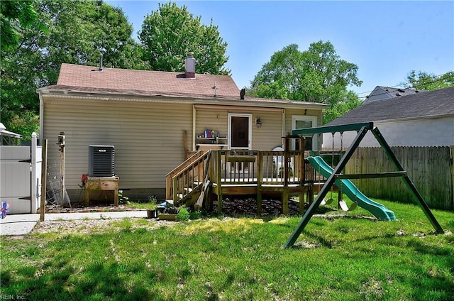 back of house featuring a lawn, a deck, fence, a playground, and a shingled roof