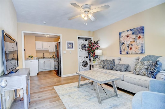 living area with stacked washing maching and dryer, baseboards, ceiling fan, and light wood-style flooring
