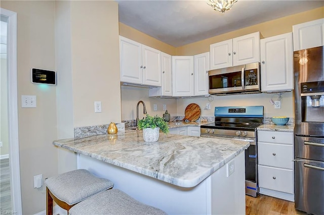 kitchen with white cabinets, stainless steel appliances, light stone countertops, and a peninsula