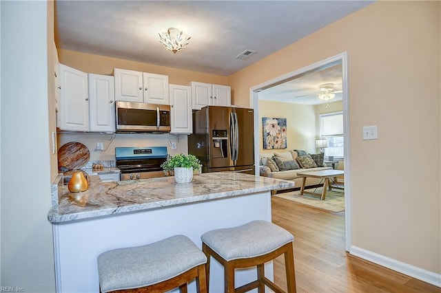 kitchen with a peninsula, light stone countertops, baseboards, white cabinets, and appliances with stainless steel finishes