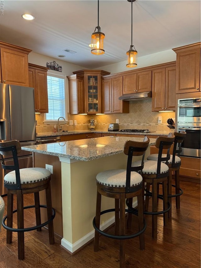 kitchen with brown cabinets, under cabinet range hood, a kitchen island, and stainless steel appliances