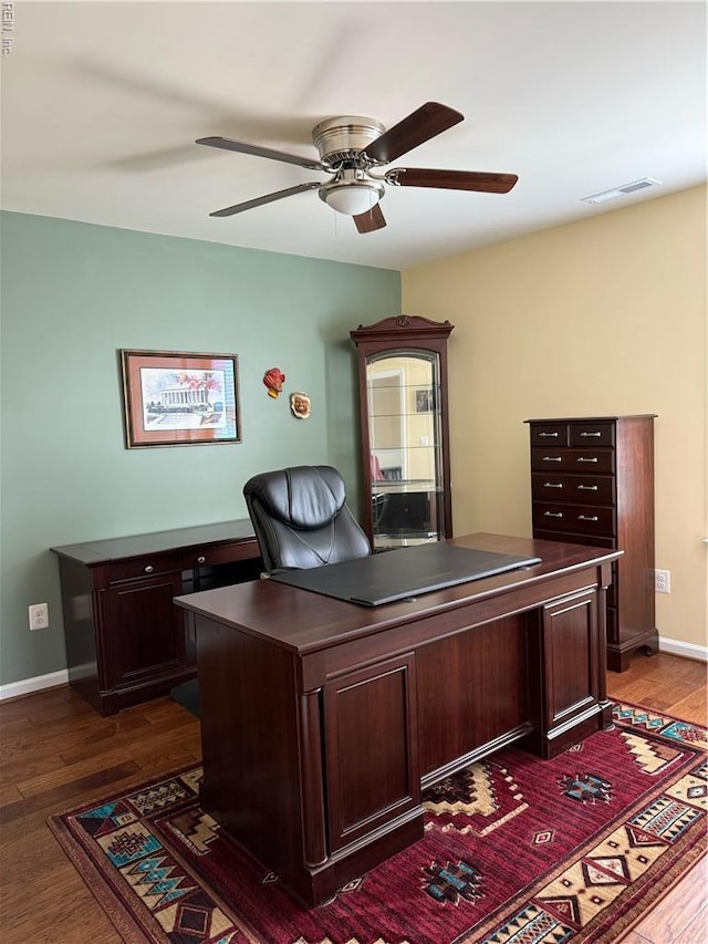 home office with ceiling fan, visible vents, dark wood-style floors, and baseboards